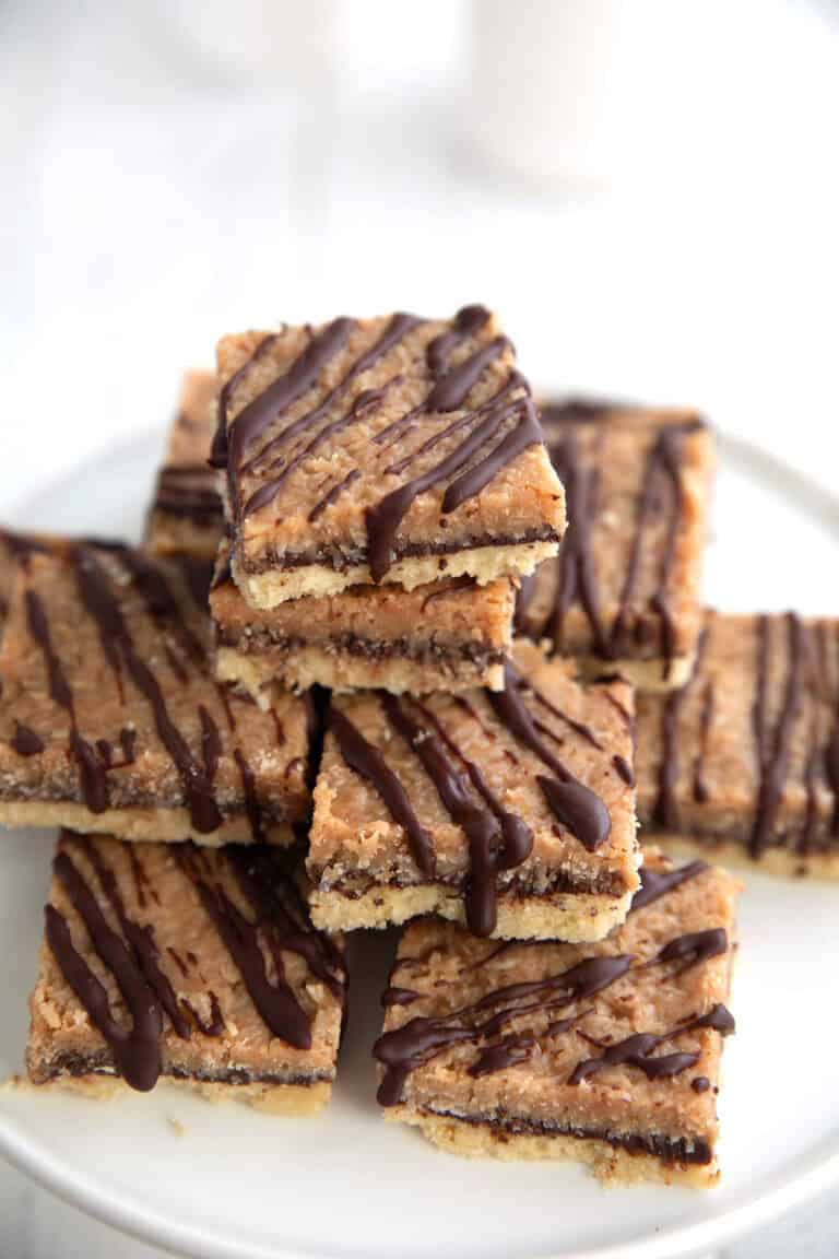 Keto Samoa Cookie Bars piled up on a white cake stand on a white table.