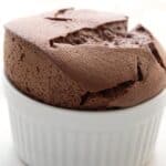 Titled image of a tall keto chocolate soufflé in a white ramekin on a white plate.