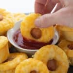 Titled image of a hand dipping a keto corn dog bite into a small bowl of sugar-free ketchup.