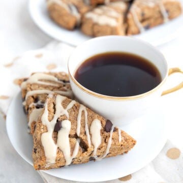 Two keto espresso scones on a white plate with a cup of coffee, over a white and gold napkin.