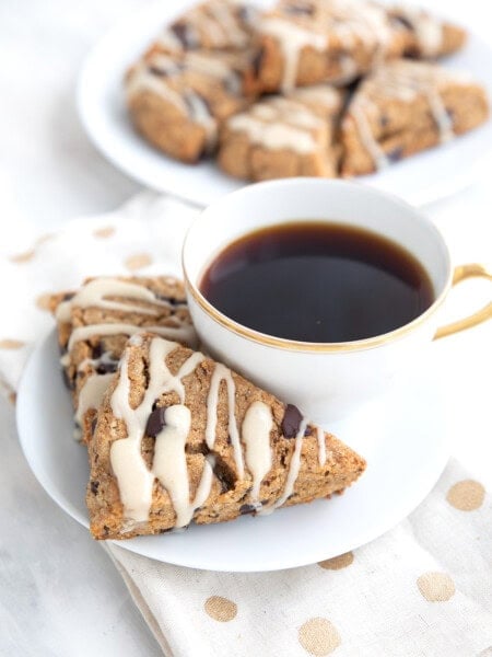 Two keto espresso scones on a white plate with a cup of coffee, over a white and gold napkin.