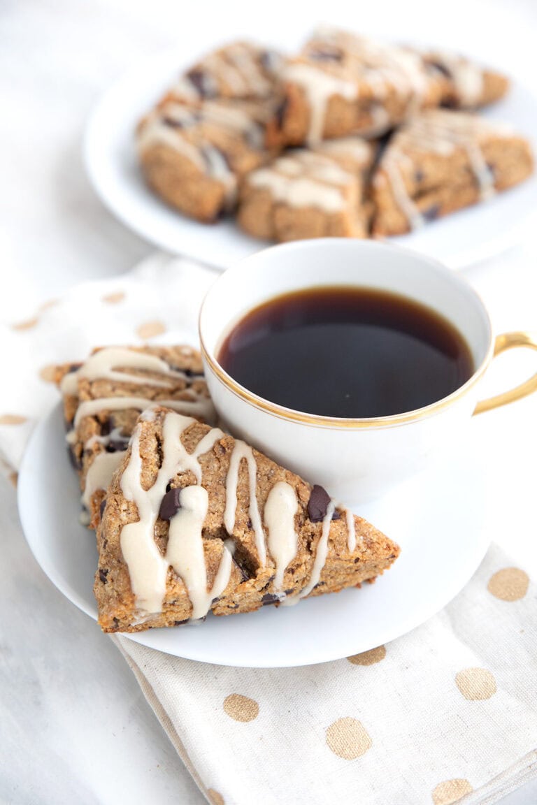 Two keto espresso scones on a white plate with a cup of coffee, over a white and gold napkin.