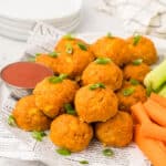 Buffalo Chicken Meatballs piled up on a white plate with carrots and celery sticks.