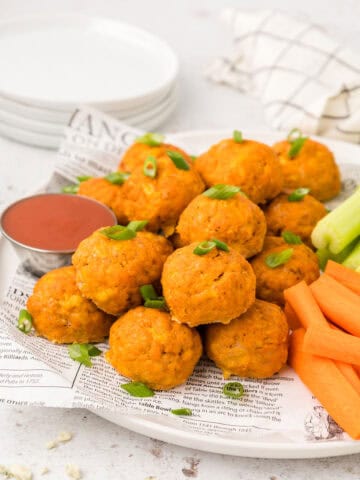 Buffalo Chicken Meatballs piled up on a white plate with carrots and celery sticks.