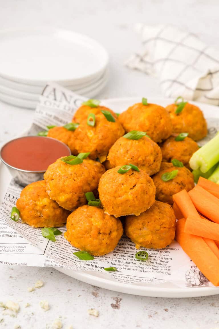 Buffalo Chicken Meatballs piled up on a white plate with carrots and celery sticks.