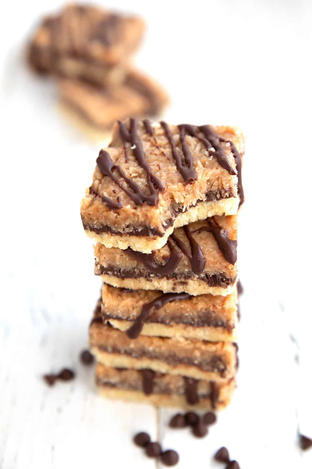 A stack of Keto Samoa Bars on a white table with chocolate chips around the bottom.