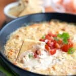 Titled image of baked shrimp dip in a bowl with a cracker dipping into it.