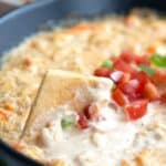 A close up shot of a cracker dipping into a black bowl filled with shrimp dip.