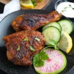 Two pieces of Air Fryer Tandoori Chicken on a black plate with sliced cucumber and watermelon radish.