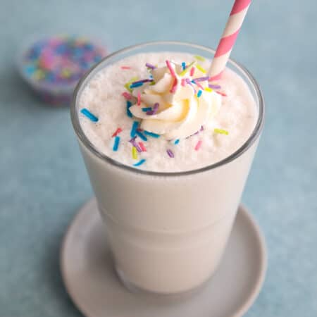 A glass filled with vanilla protein shake with whipped cream and sprinkles on top.