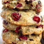 Titled image of a stack of protein breakfast cookies on a pink-hued table with cranberries and chocolate chips around the base.