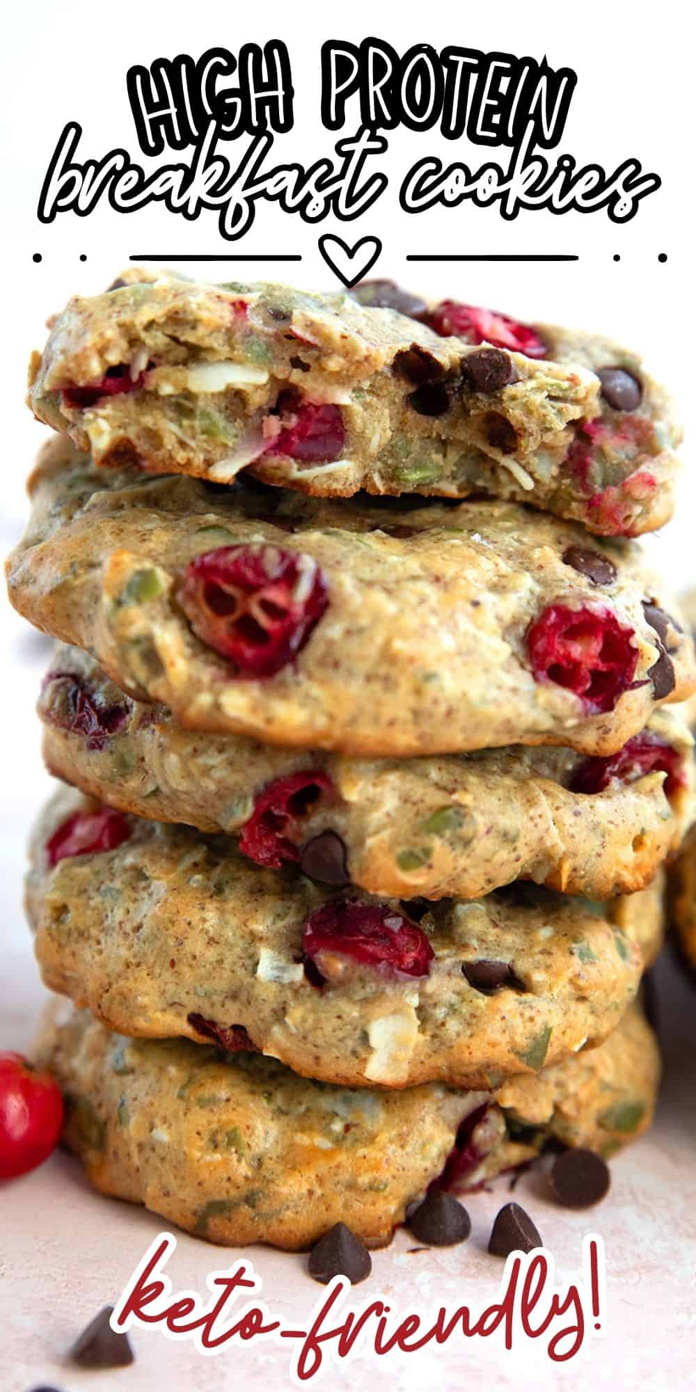 Titled image of a stack of protein breakfast cookies on a pink-hued table with cranberries and chocolate chips around the base.