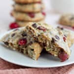 Close up shot of a Protein Breakfast Cookie broken in half on a white plate over a dark pink napkin.