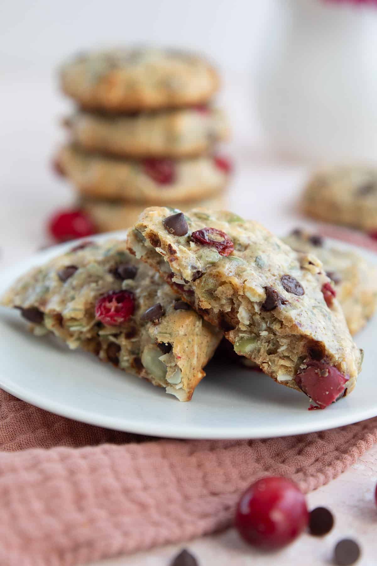 Close up shot of a Protein Breakfast Cookie broken in half on a white plate over a dark pink napkin.