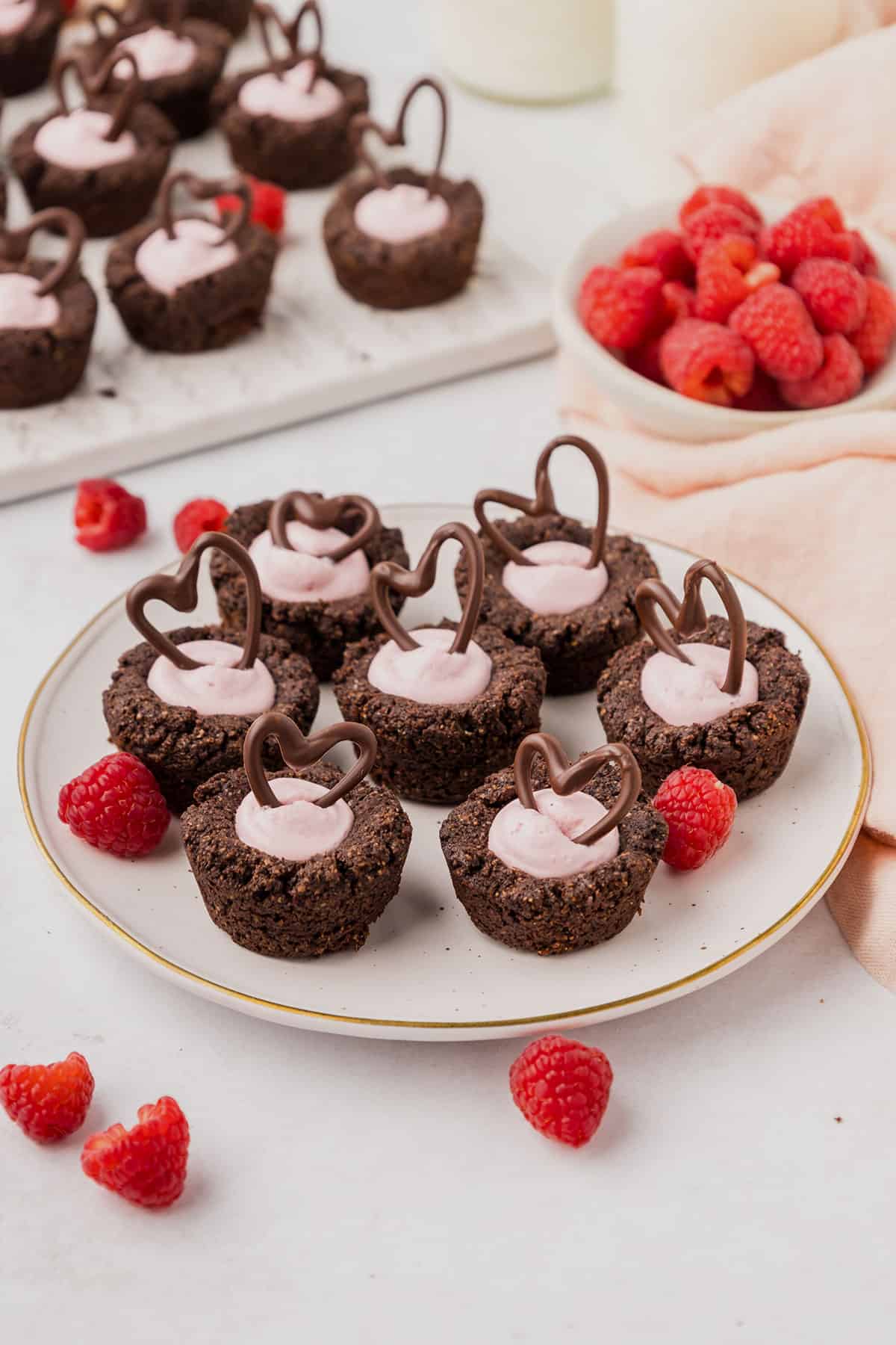 Keto Raspberry Cheesecake Cookie Cups on a white plate on a white table, with fresh raspberries strewn around.