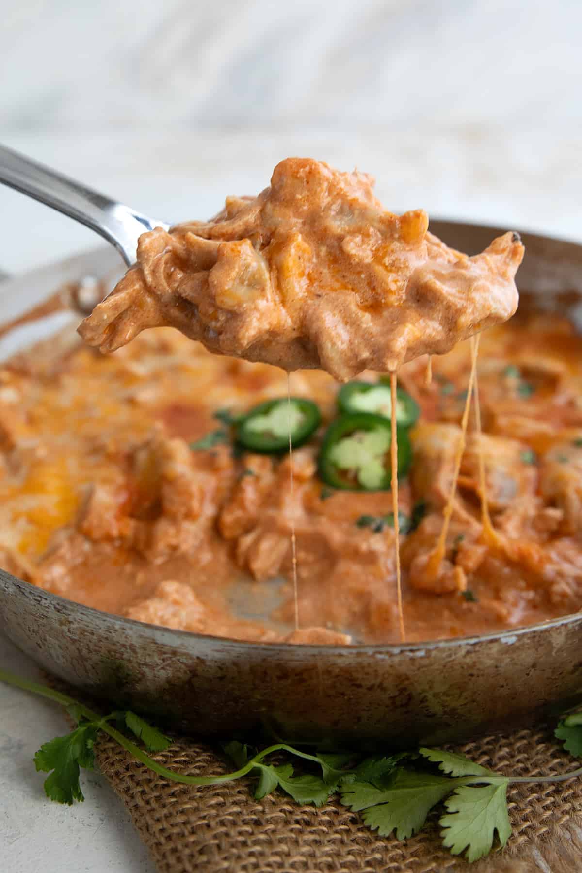 A metal serving spoon lifts a serving of Chicken Enchilada Skillet from a metal pan.