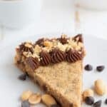 Titled image of Keto Peanut Butter Cookie Cake on a white plate with peanuts and chocolate chips.