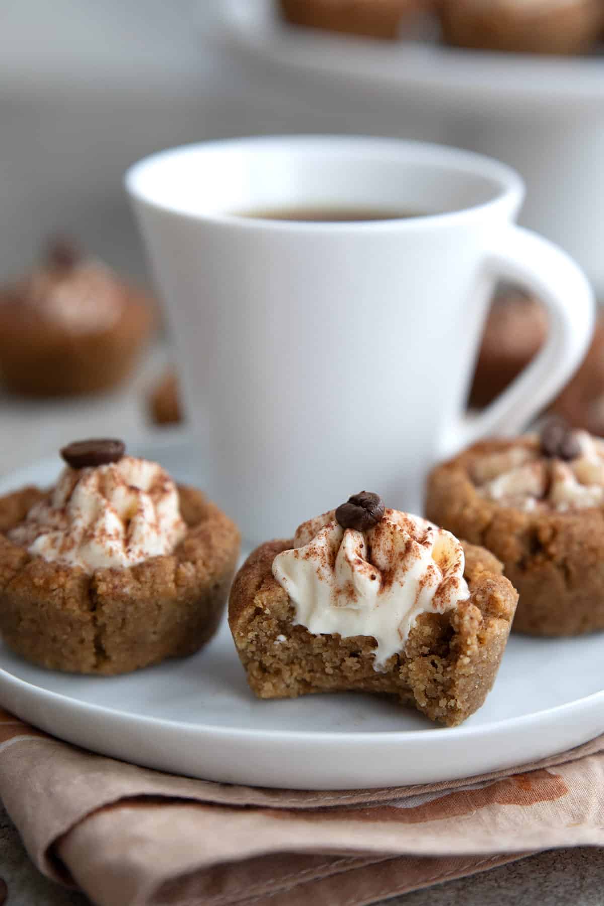 Keto Tiramisu Cookie Cups on a white plate with a small cup of coffee, with a bite taken out of the front one.