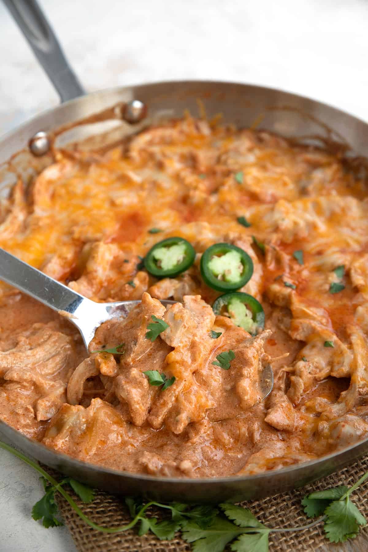 A metal serving spoon digging into a pan filled with Chicken Enchilada Skillet.