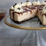 Keto Irish Cream Cheesecake on a glass cake stand with a slice cut out of it.