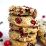 A stack of Protein Breakfast Cookies on a pink-hued table with fresh cranberries and chocolate chips strewn around.