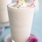 A tall glass filled with vanilla protein shake with a pink striped straw stuck into it.