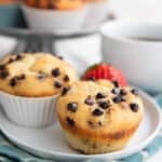 Two keto muffins with chocolate chips on top sitting on a white plate over a teal plaid napkin.