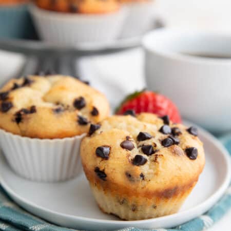 Two keto muffins with chocolate chips on top sitting on a white plate over a teal plaid napkin.