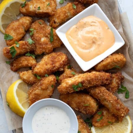 Top down image of air fryer fish sticks on a metal tray lined with parchment paper.