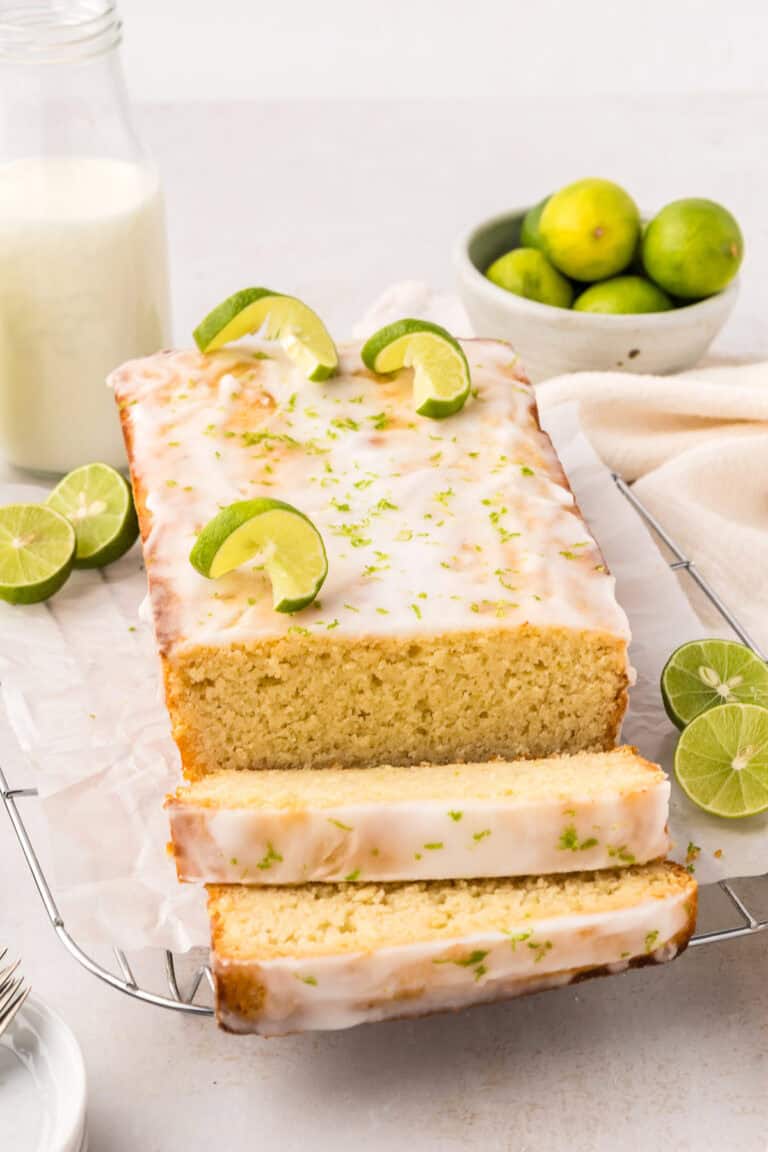 A loaf of Keto Key Lime Pound Cake on a wire cooling rack with several slices cut out in front.