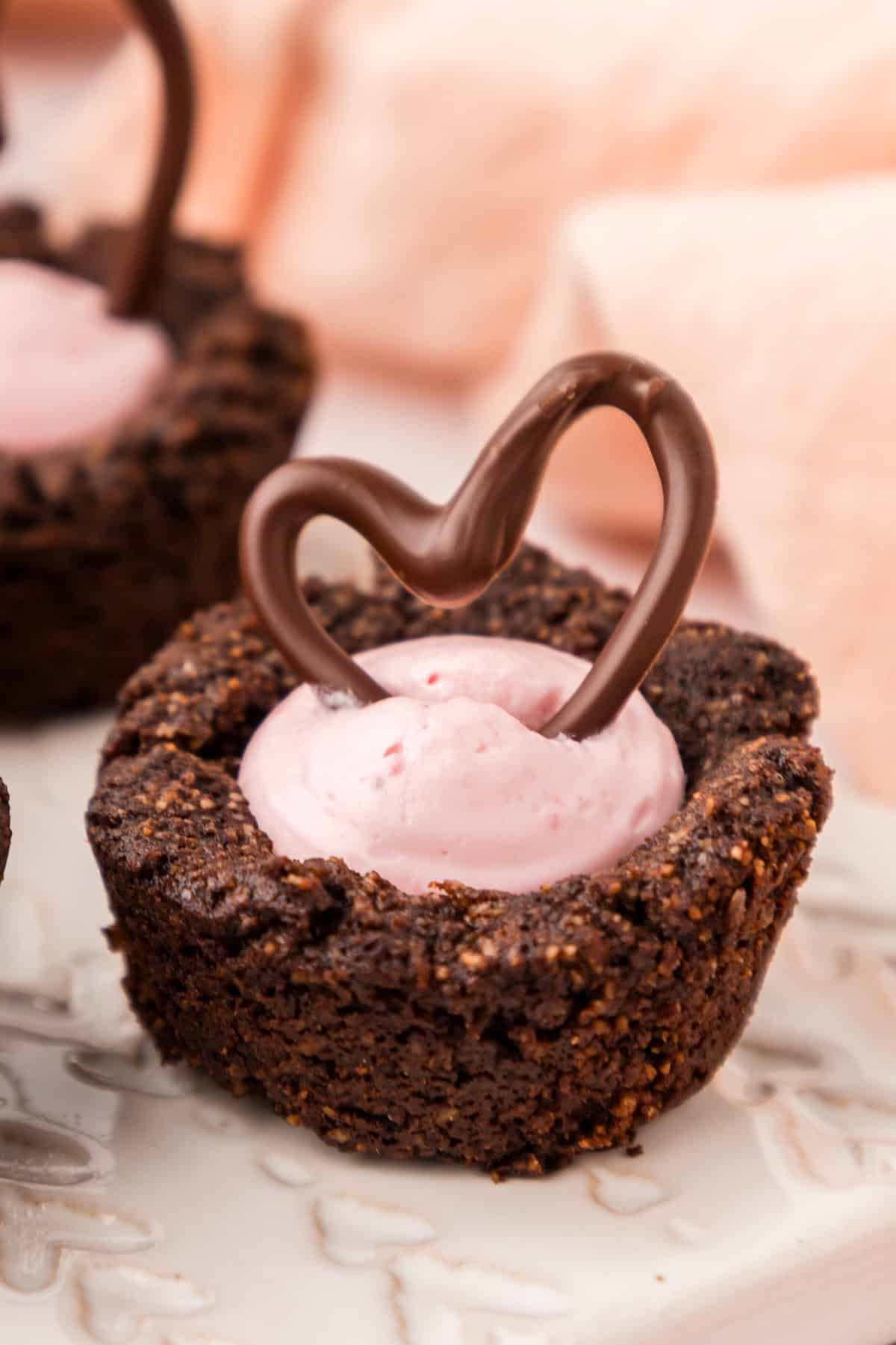 Close up shot of a Keto Raspberry Cheesecake Cookie Cups on a white plate with a chocolate heart on top.