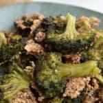 Titled image of smashed broccoli piled up in a green rustic dish.