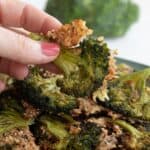 A hand holding up a piece of smashed broccoli above a bowl of more broccoli.