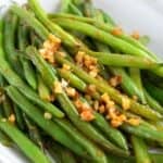 Titled image close up of a white bowl filled with spicy Chili Garlic Green Beans.