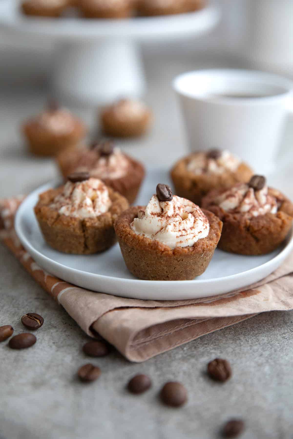 Five Keto Tiramisu Cookie Cups on a small white dessert plate over a beige napkin.