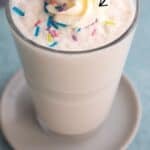 Titled image of a vanilla protein shake in a tall glass with whipped cream and sprinkles on top.