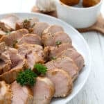 Sliced garlic keto pork tenderloin arranged on a white plate on a white wooden table.