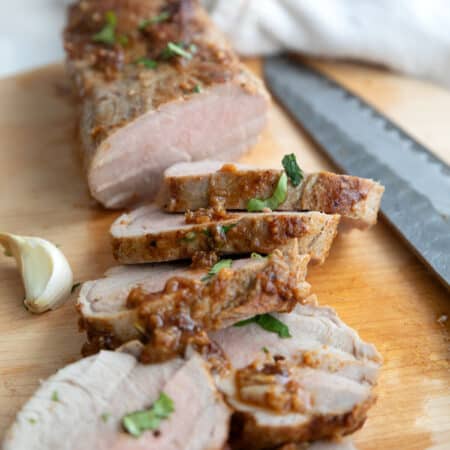 Keto pork tenderloin sliced on a cutting board with pan sauce and chopped cilantro.