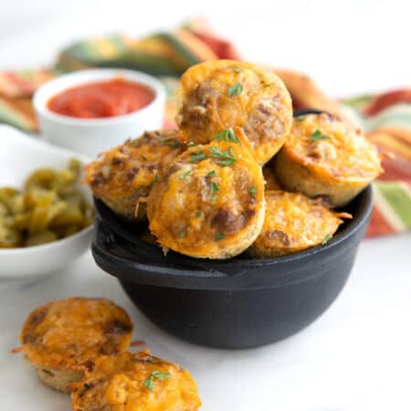 Keto Taco Bites piled up in a black cast iron dish, with two sitting in front.