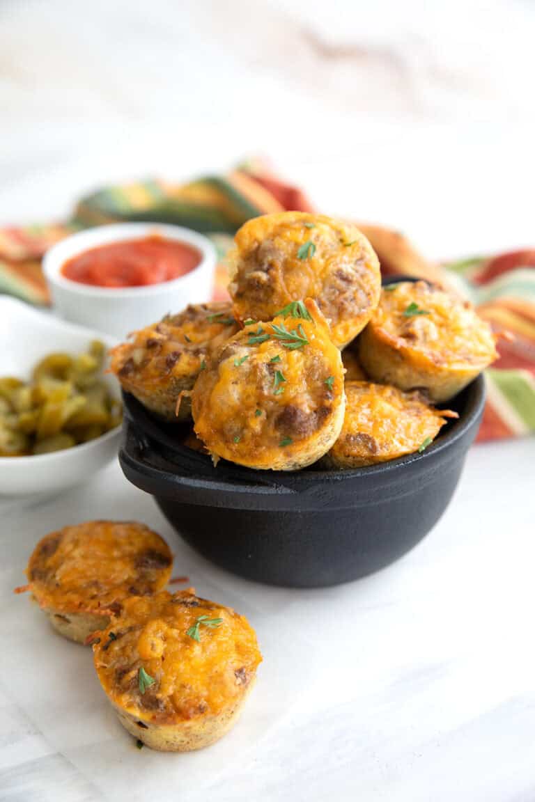 Keto Taco Bites piled up in a black cast iron dish, with two sitting in front.