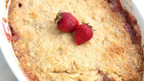 Keto Strawberry Rhubarb Dump Cake in a white oval dish on a white tabletop, with a scoopful cake out of it.