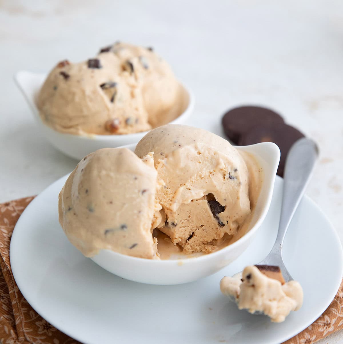 Two white bowls filled with peanut butter frozen yogurt with a spoonful taken out of one.