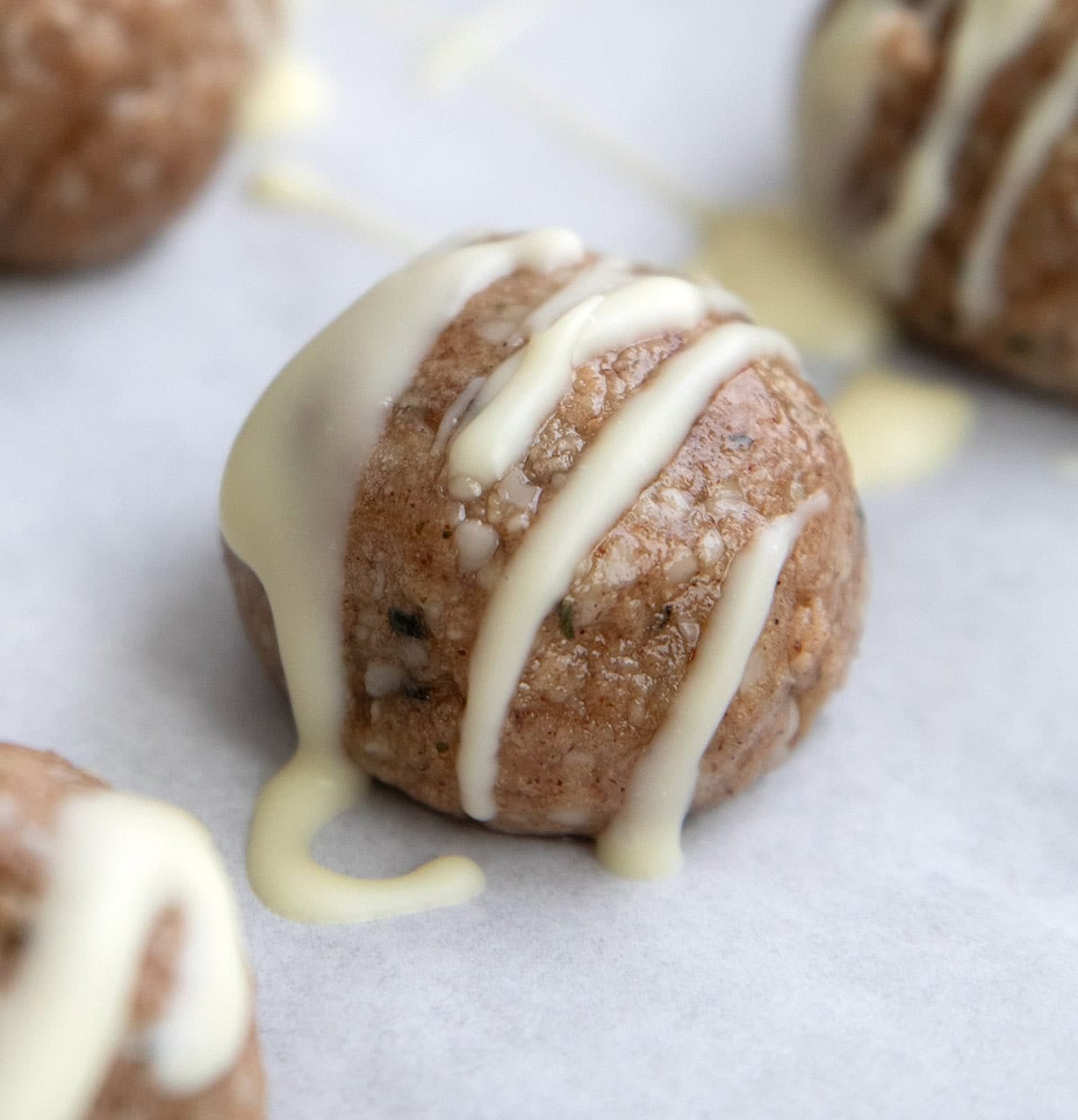 Close up shot of a Cinnamon Roll Protein Bite with white chocolate drizzle on white parchment paper.