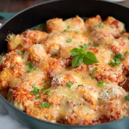 A large cast iron skillet full of chicken parmesan meatballs with chopped basil.