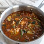 Hearty keto minestrone soup in a stainless steel soup pot on a white table.