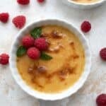 Top down image of keto creme brûlée in a white ramekin with raspberries all around it.