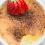 Titled image top down of keto creme brûlée in a shallow white ramekin with a strawberry on top.