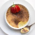 Top down image of keto creme brûlée in a shallow white ramekin with a strawberry on top.