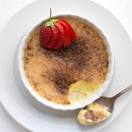 Top down image of keto creme brûlée in a shallow white ramekin with a strawberry on top.