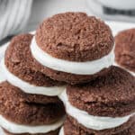 Keto Gingerbread Whoopie Pies piled up on a white plate with a glass of milk in the background.